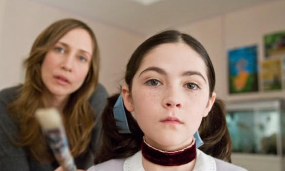 A young girl stares with her mother behind her looking on.