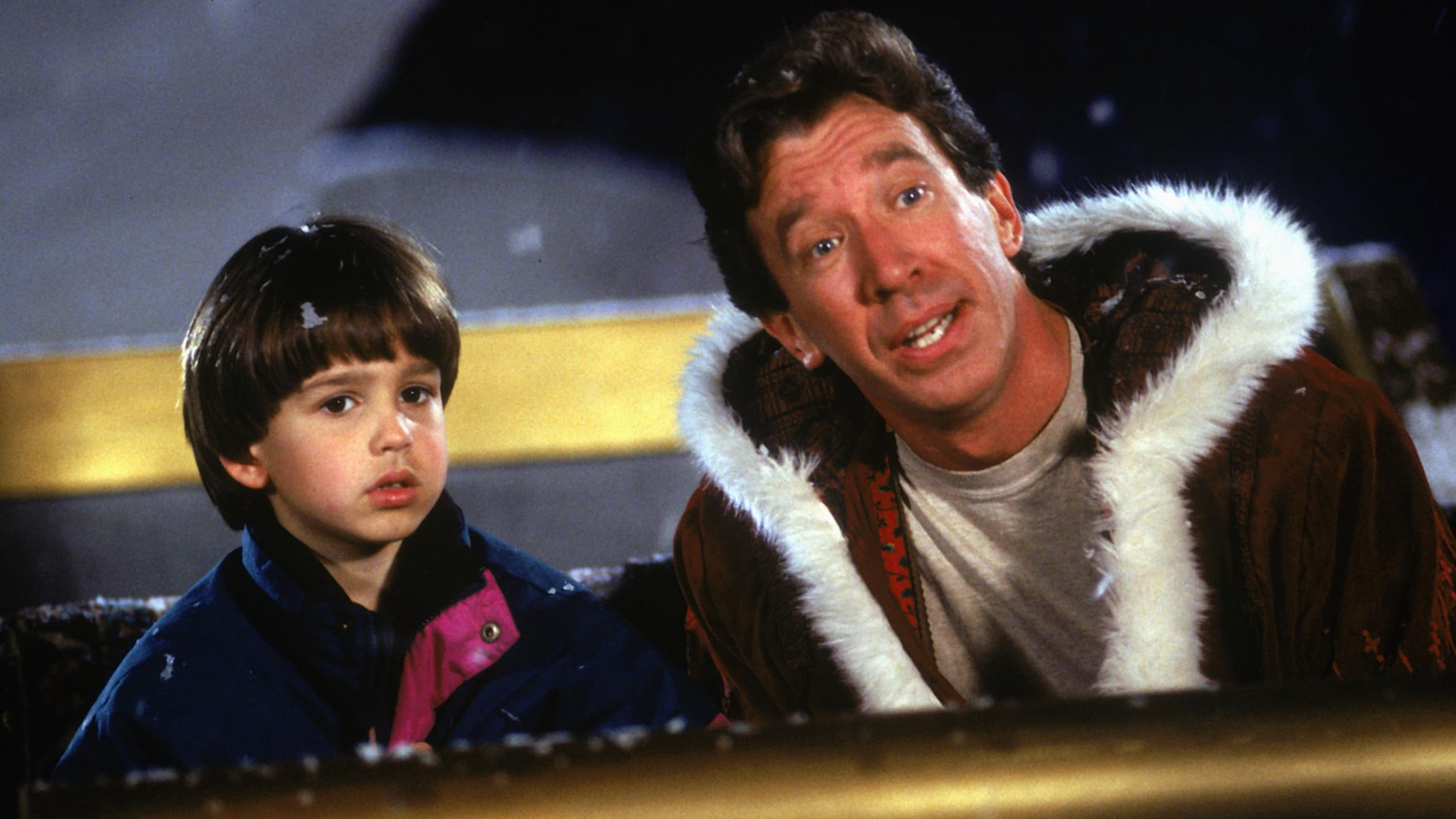 Tim Allen sits in a sleigh with a boy.