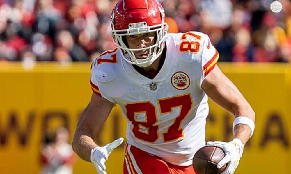 Travis Kelce holds the ball with one hand and runs.