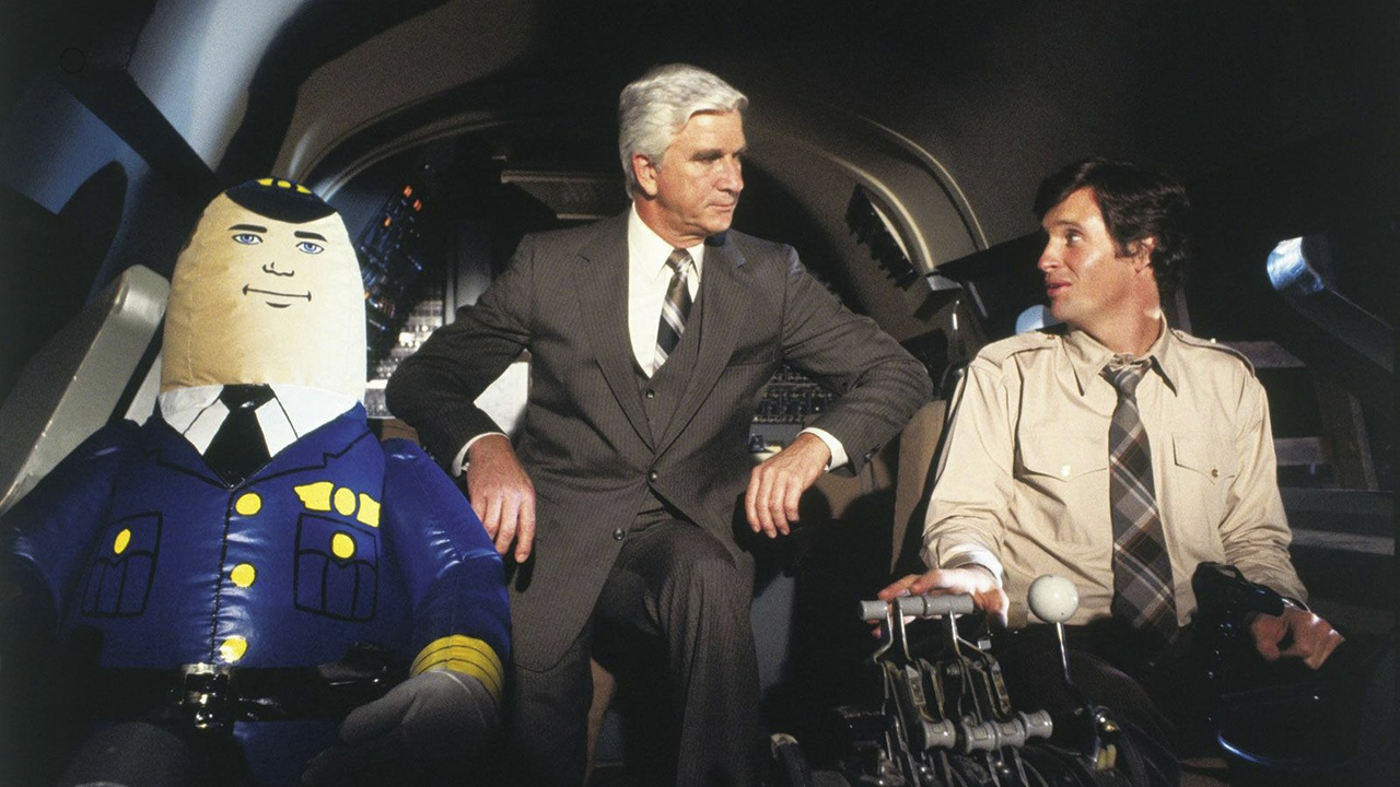 Two men sitting in a plane's cockpit with a blow-up in a pilot outfit in Airplane!