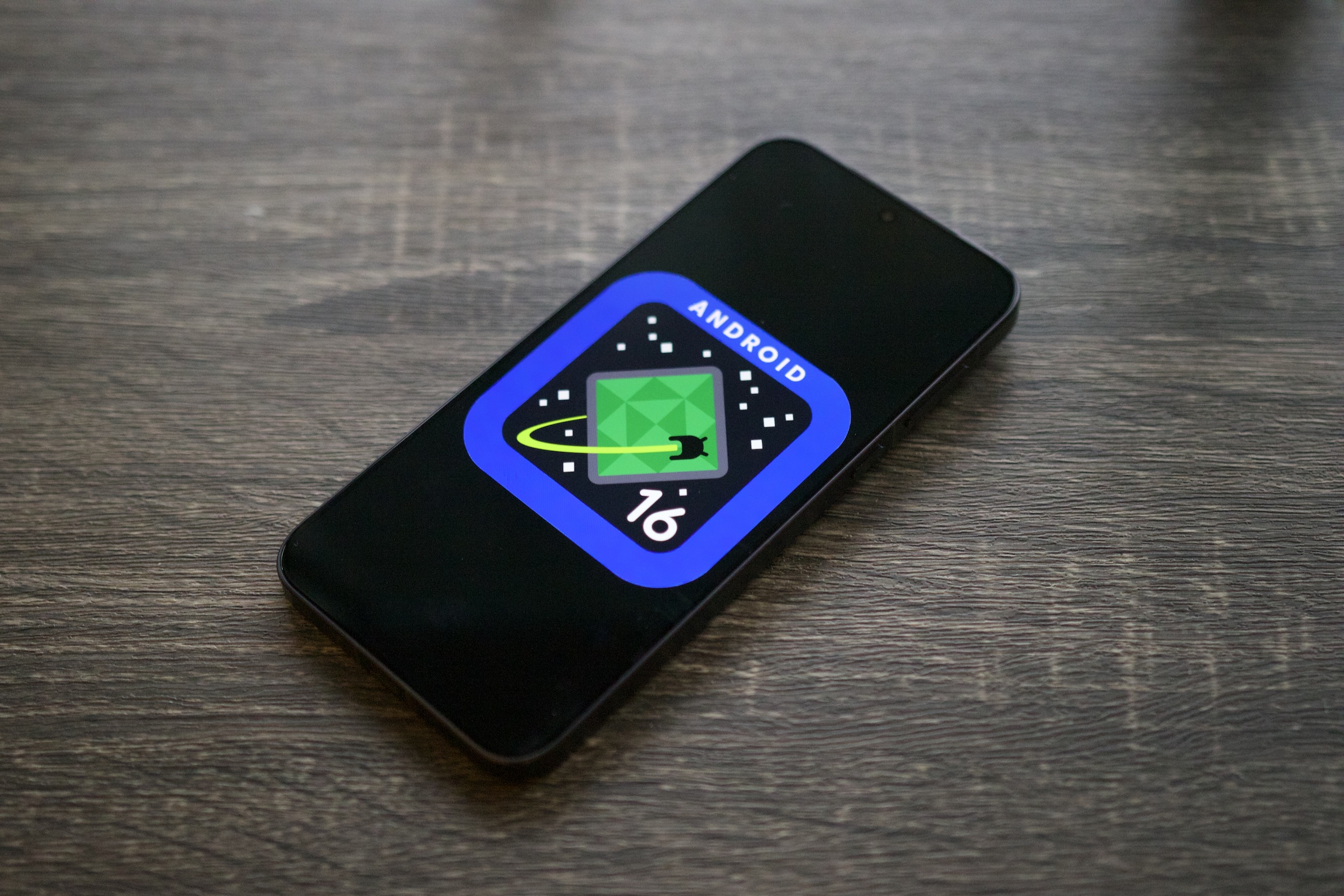 El logotipo de Android 16 en un teléfono inteligente, apoyado en un estante.