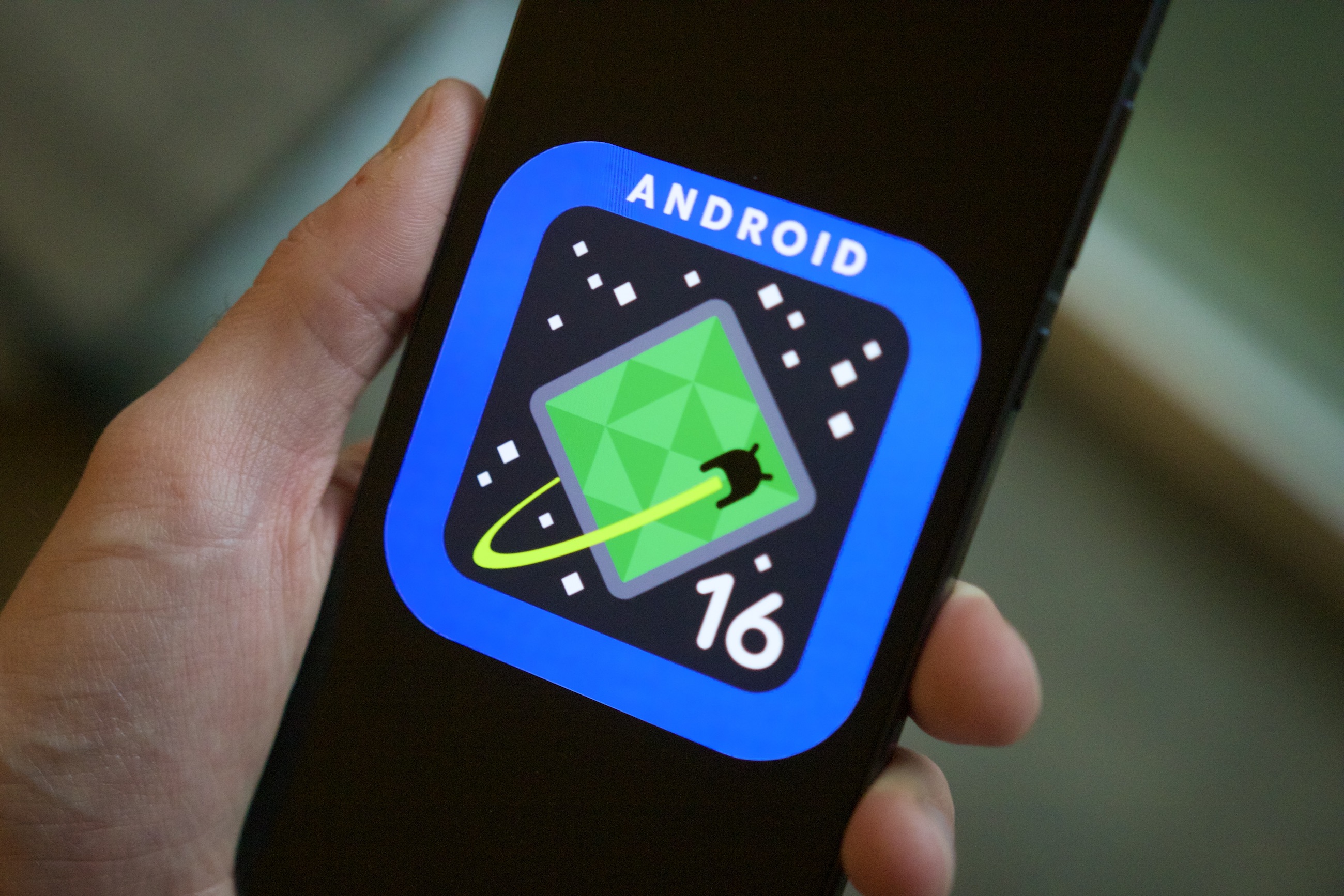 Alguien sosteniendo un teléfono que muestra el logotipo de Android 16 en su pantalla.