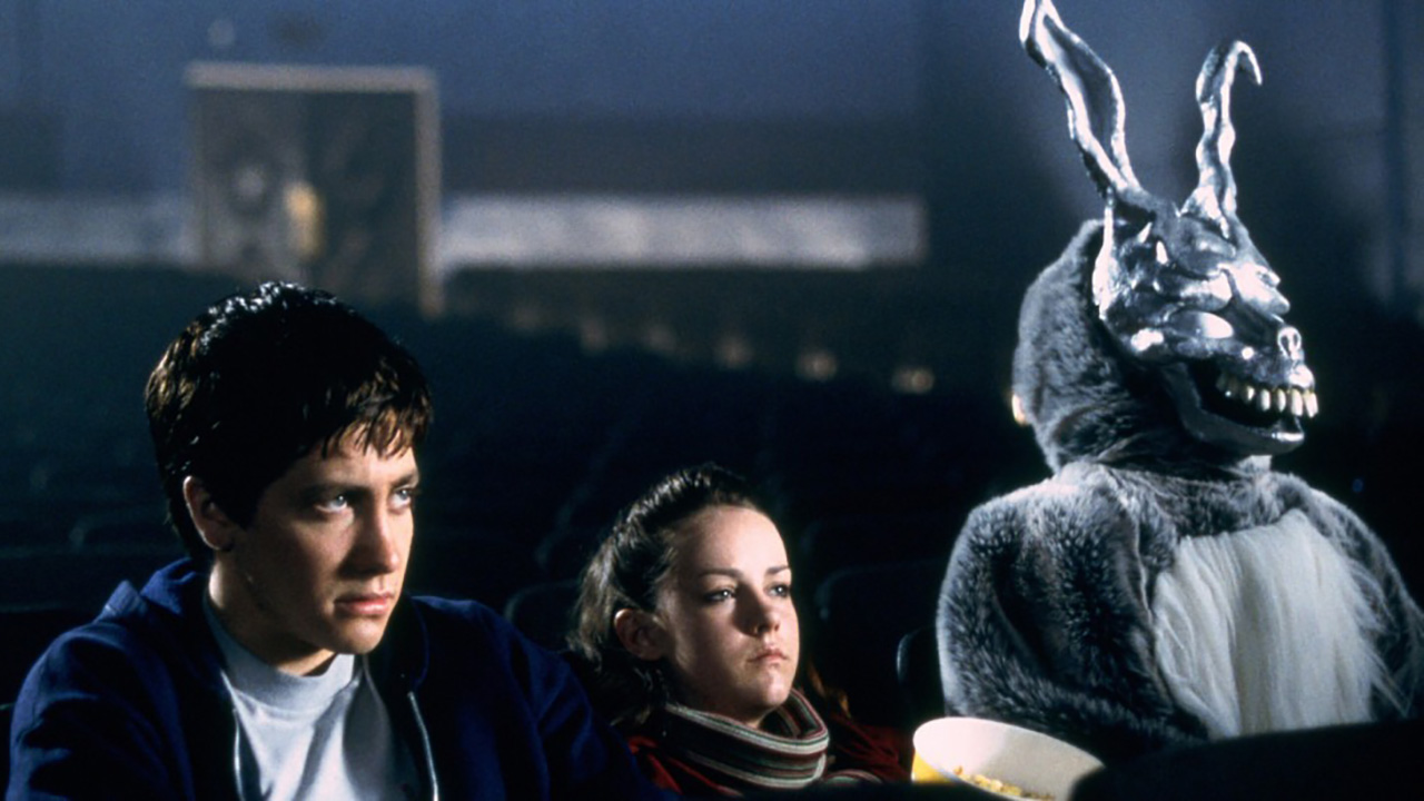 Um jovem, uma menina e um homem vestido de coelho estão sentados em uma sala de cinema em Donnie Darko.