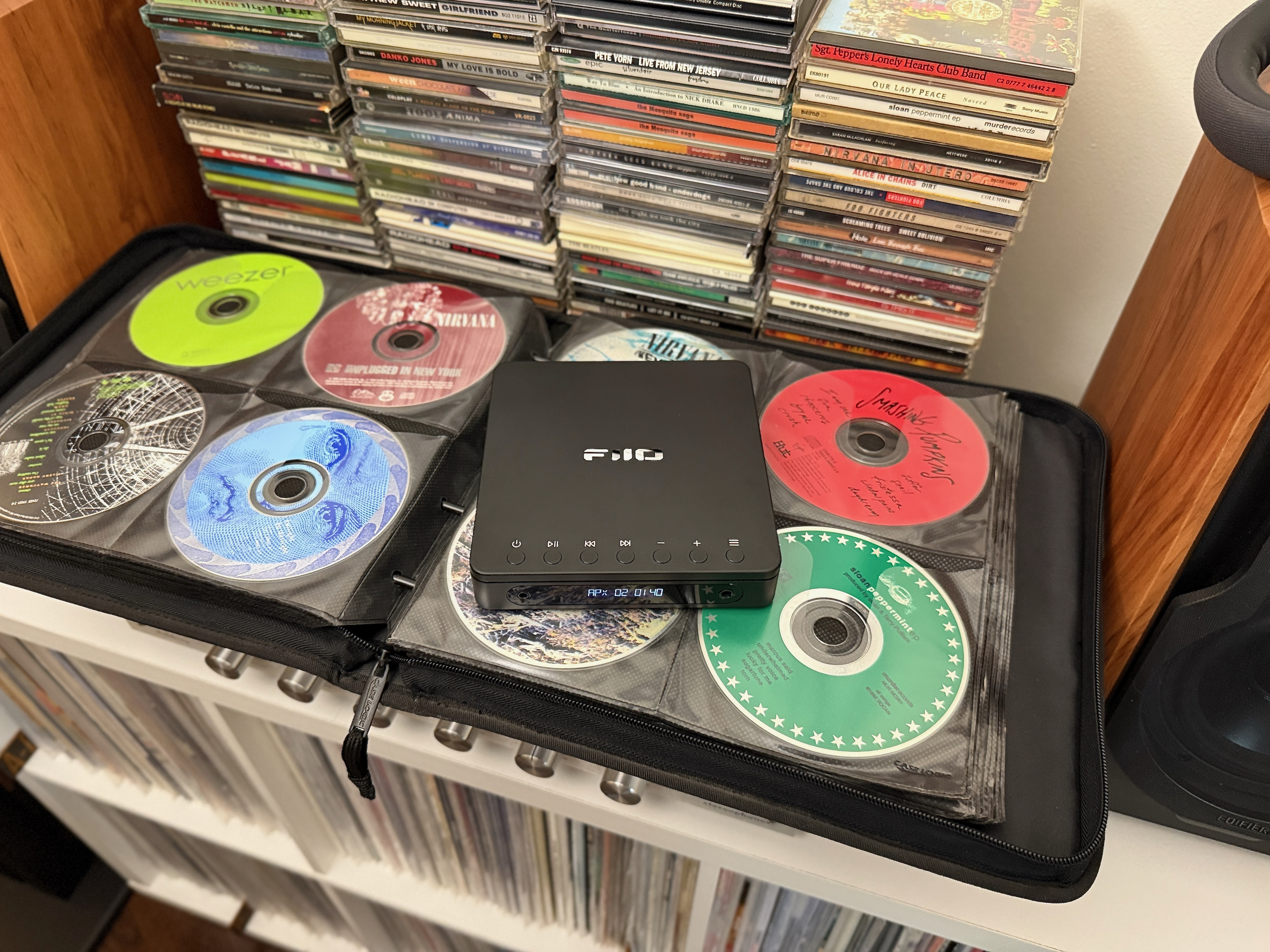 Le lecteur CD stéréo portable Fiio dm13 au-dessus d'un classeur de CD et devant des piles de CD.