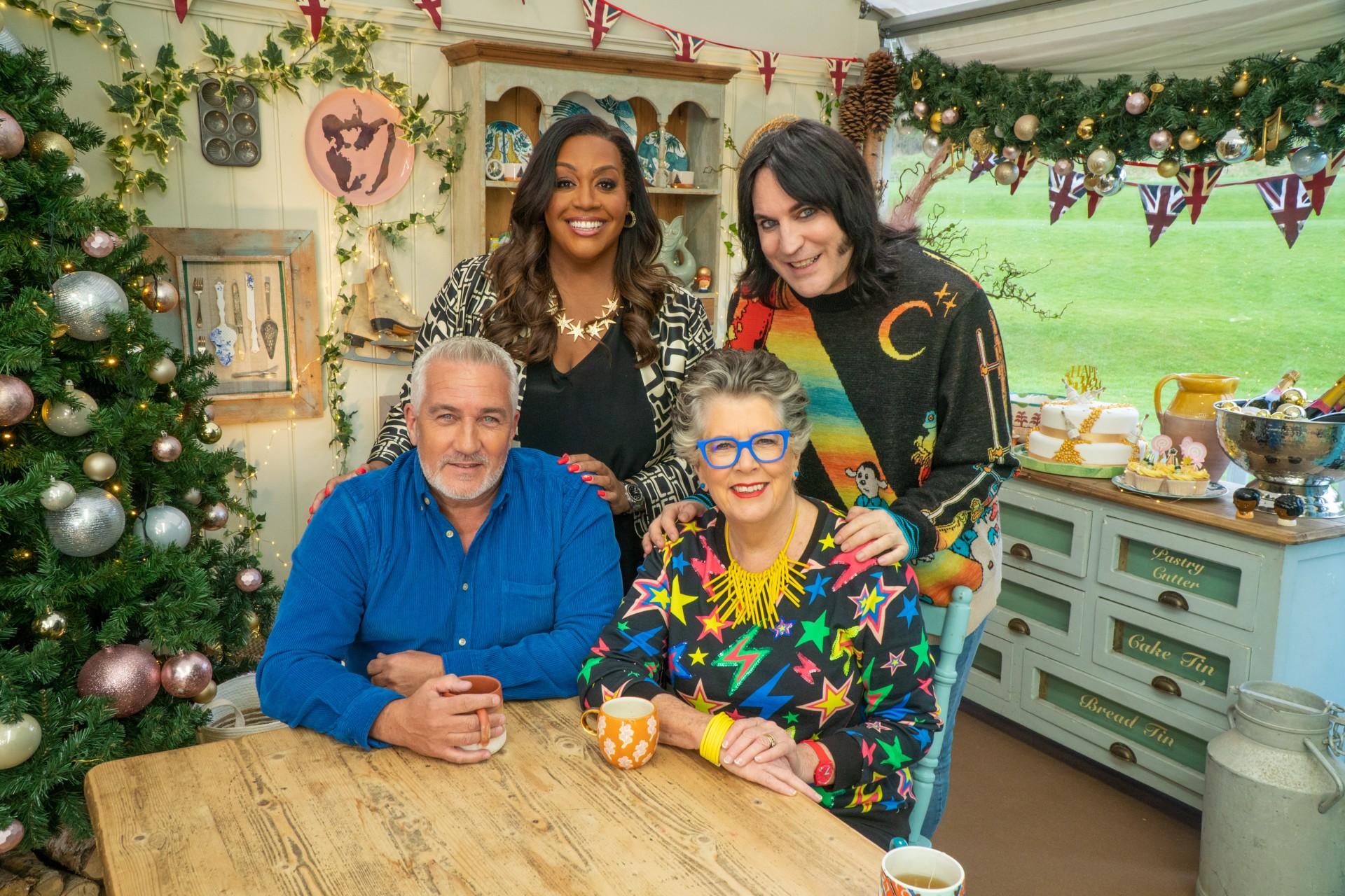 Vier Personen lächeln an einem Tisch in der Great British Baking Show Holidays.