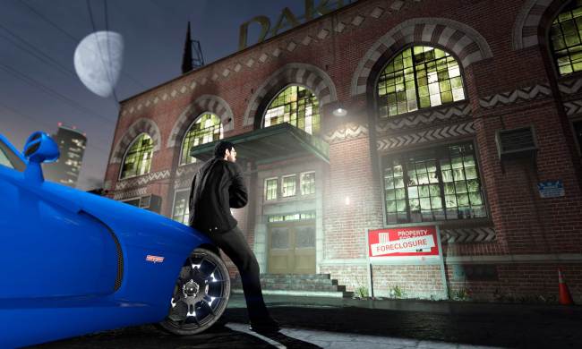 A guy leaning on a blue car in front of a big brick foreclosed building in GTA Online.