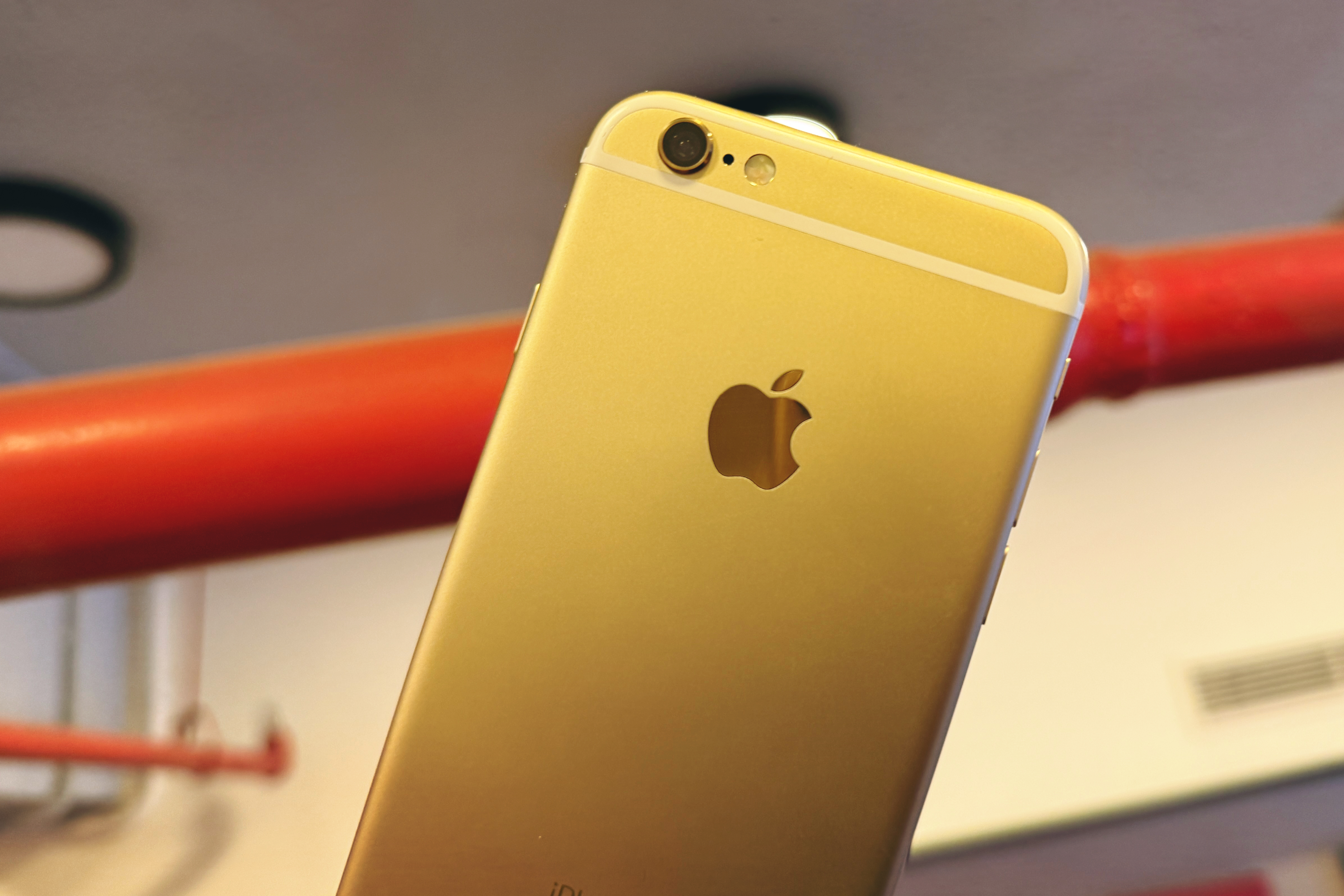 Un iPhone 6S en or tenu contre un tuyau rouge.