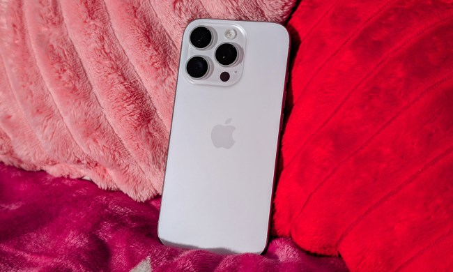 White Titanium iPhone 16 Pro sitting on blankets with heart pillows behind.