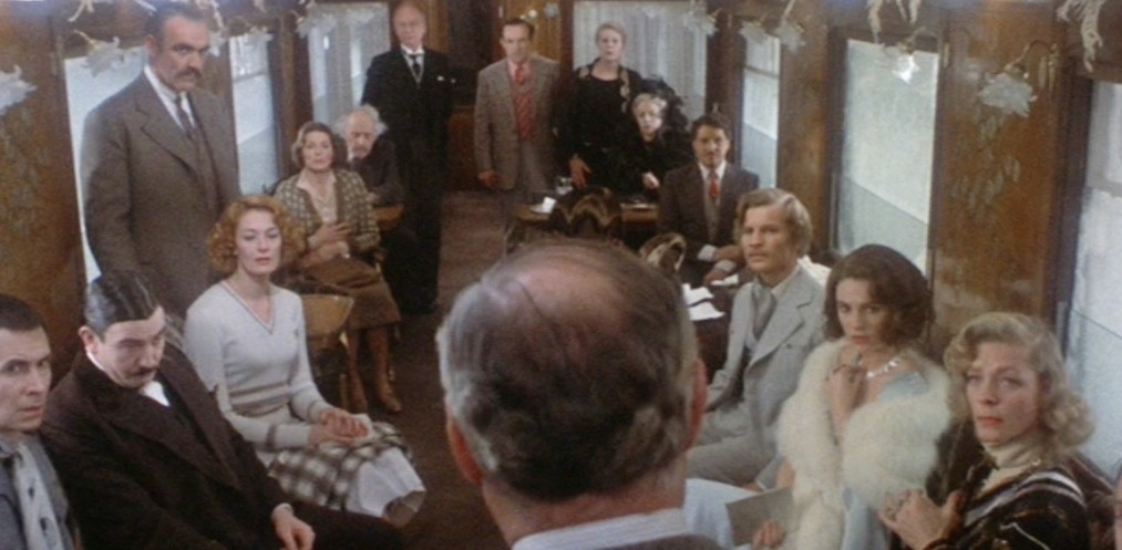 A group of people look at a man in Murder on the Orient Express.