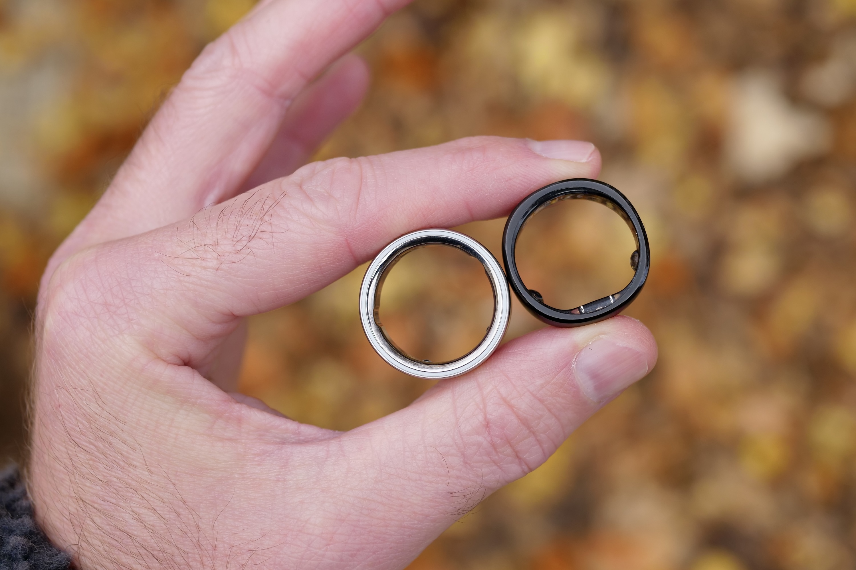 A person holding the Oura Ring 4 and the RingConn Gen 2.