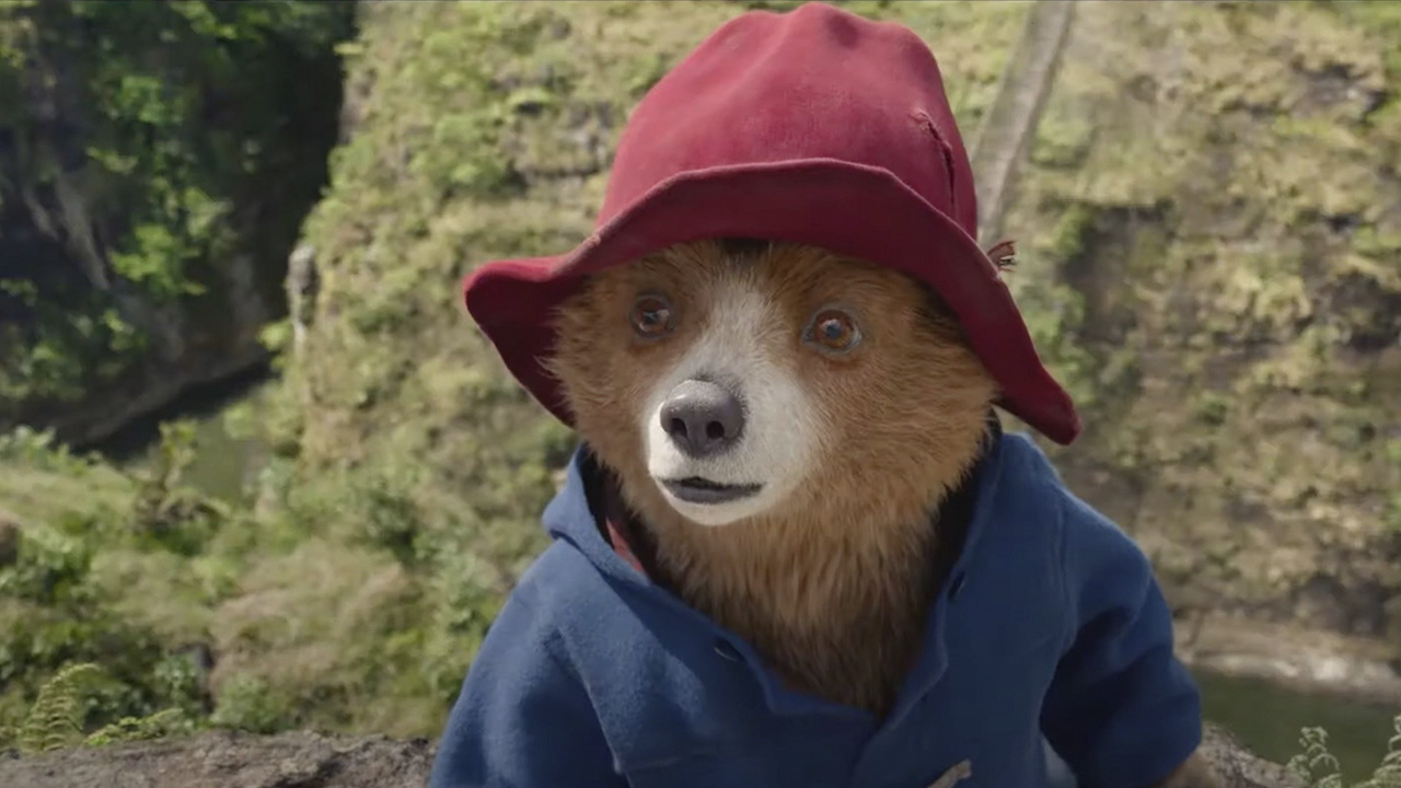 Ours Paddington levant les yeux avec un chapeau rouge et un manteau bleu à Paddington.