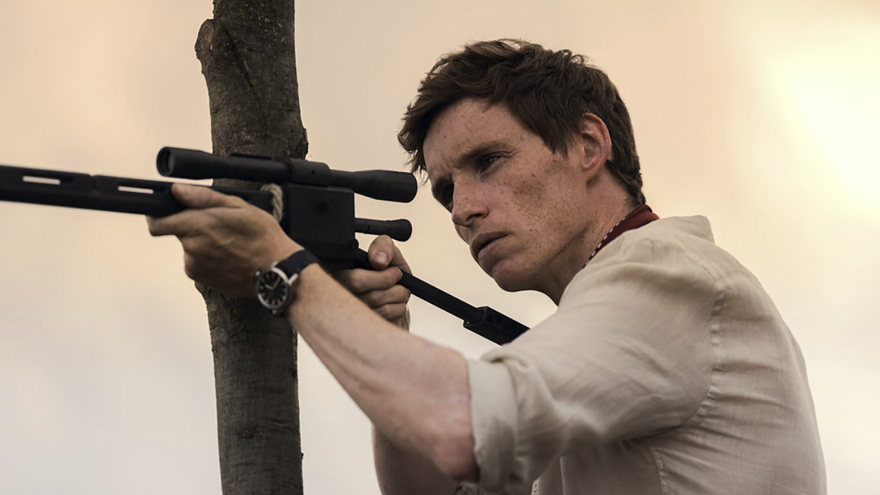 Eddie Redmayne holding out a rifle and aiming in The Day of the Jackal.