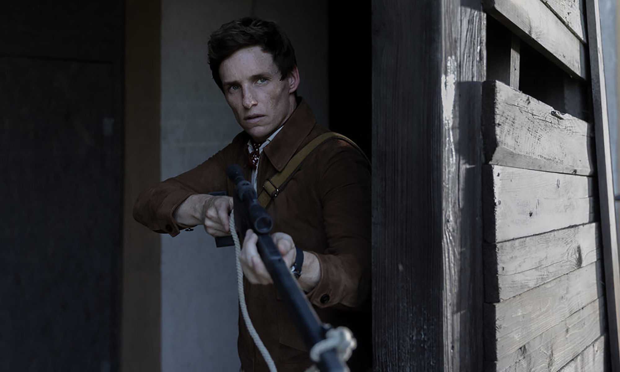 Eddie Redmayne parado junto a una puerta sosteniendo un arma en El día del chacal.