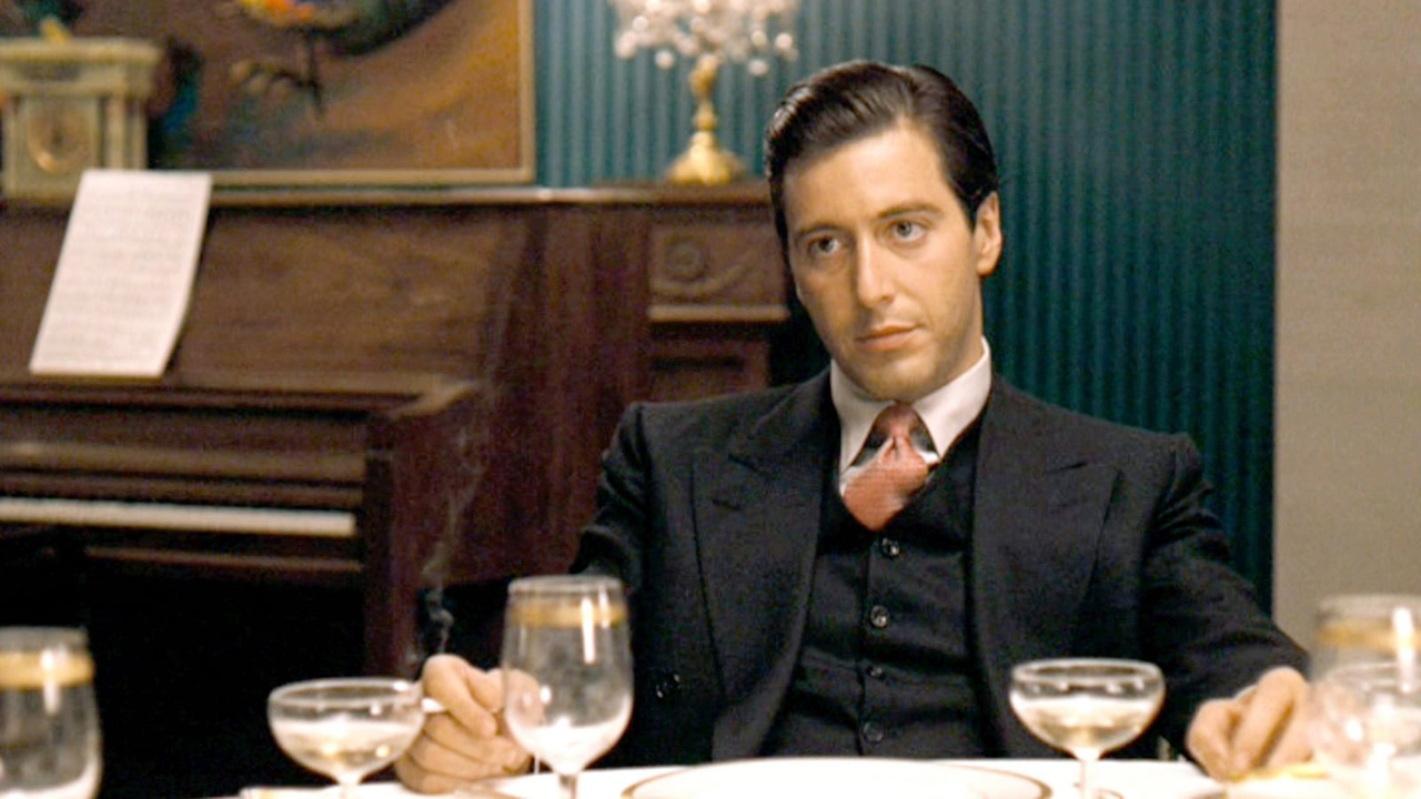 Michael Corleone sentado en un escritorio con traje en El Padrino.