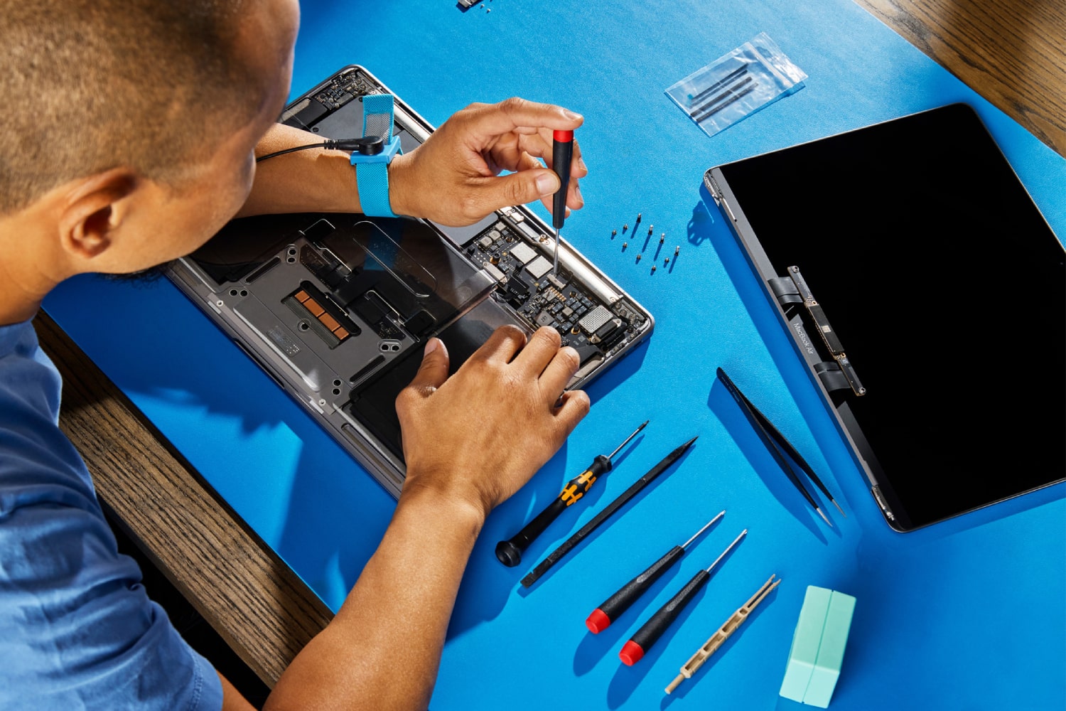 Uma pessoa consertando um MacBook em uma mesa azul.