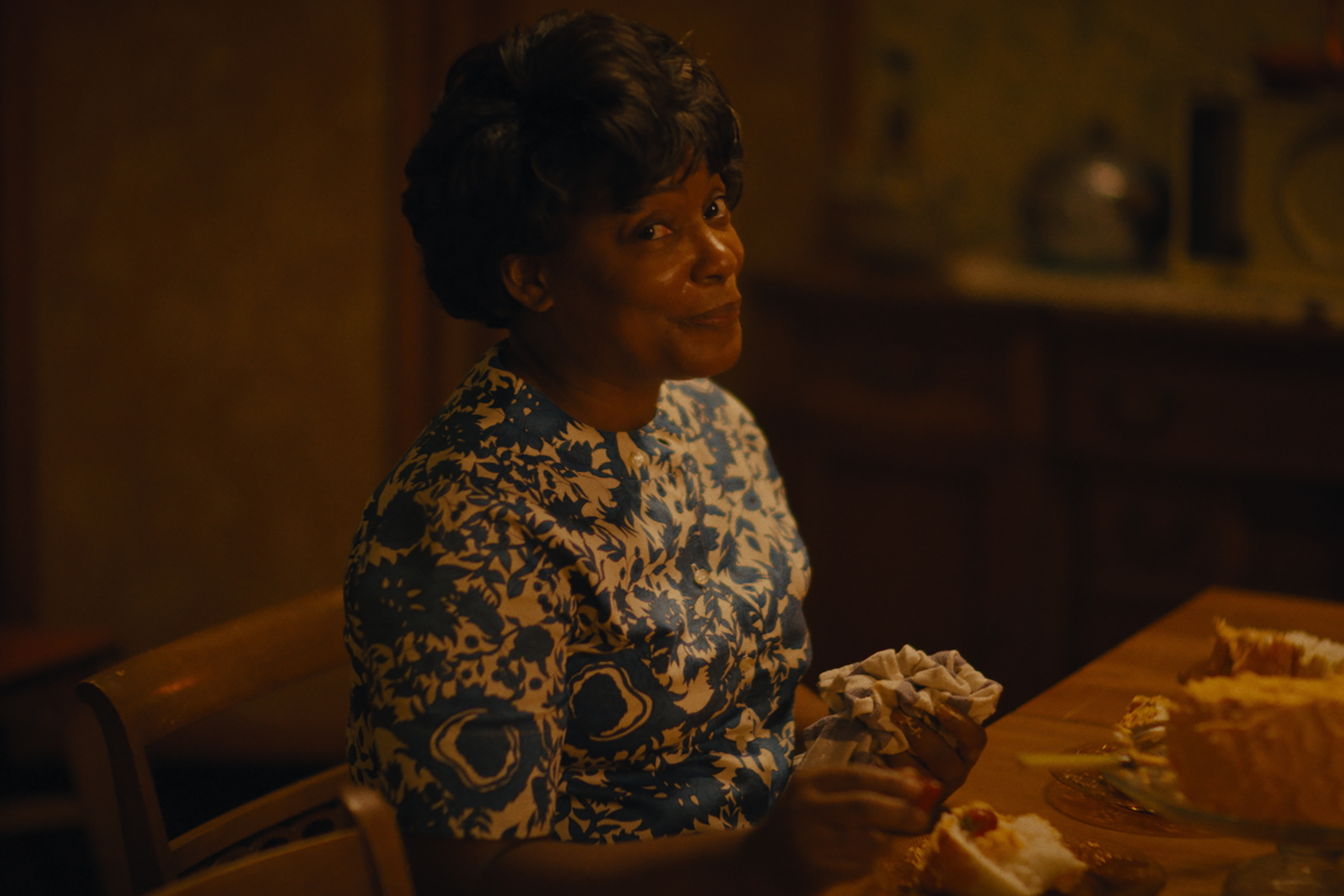 Aunjanue Ellis-Taylor sits at a dinner table in Nickel Boys.