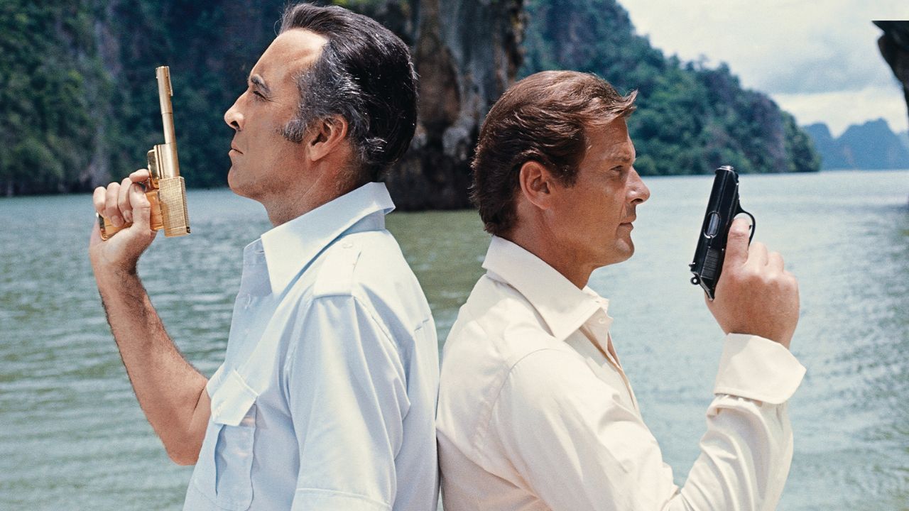 Christopher Lee e Roger Moore como Francisco Scaramaga e James Bond, lado a lado, segurando pistolas em O Homem da Pistola de Ouro.