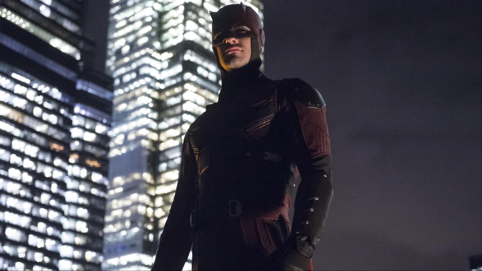 Daredevil stands on a roof with the city behind it.