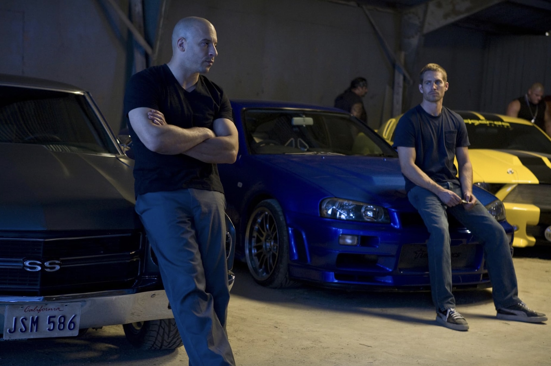 Vin Diesel and Paul Walker stand in front of their cars in Fast & Furious 4.