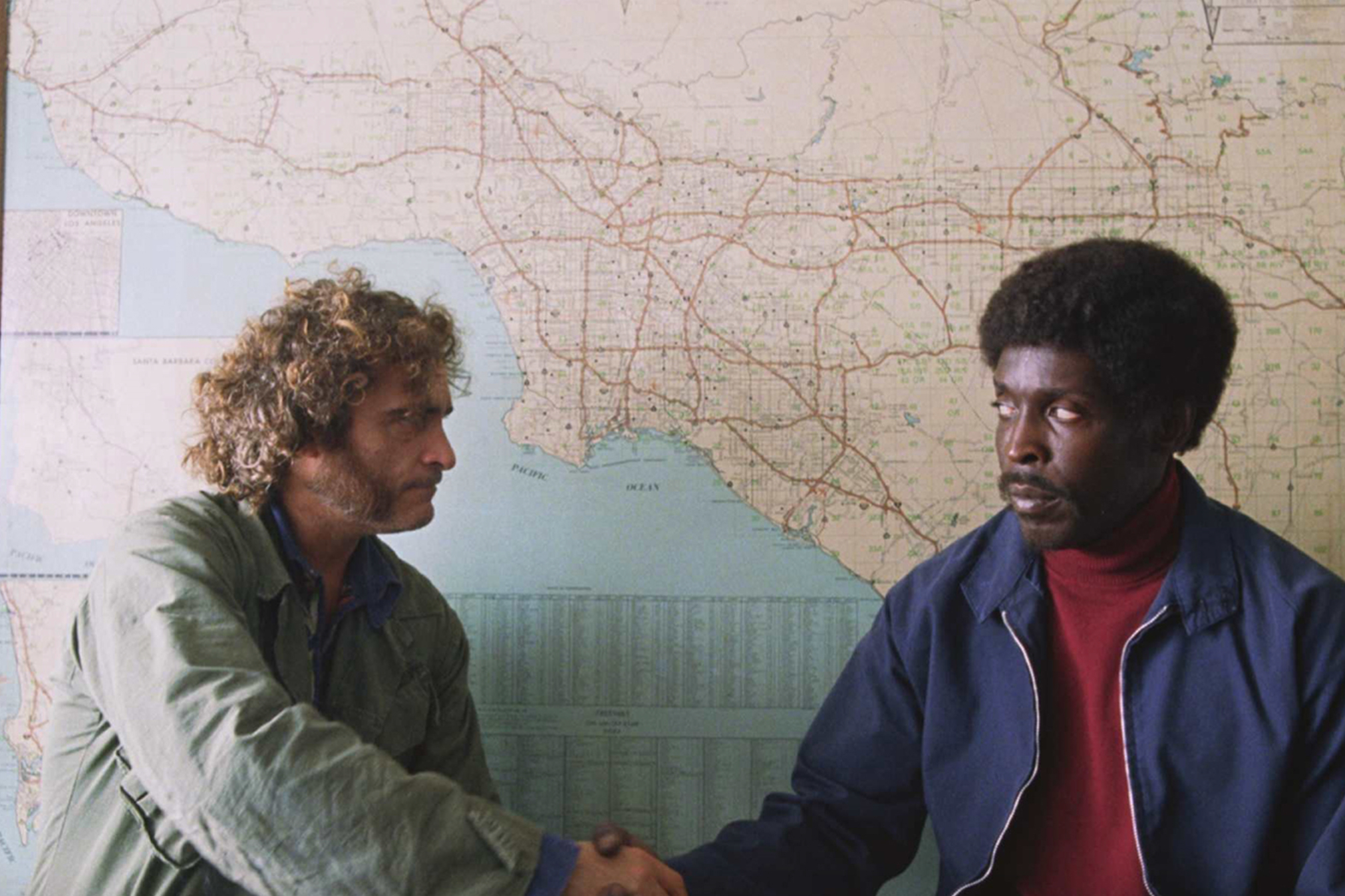 Joaquin Phoenix e Michael K. Williams estão diante de um mapa em Inherent Vice.