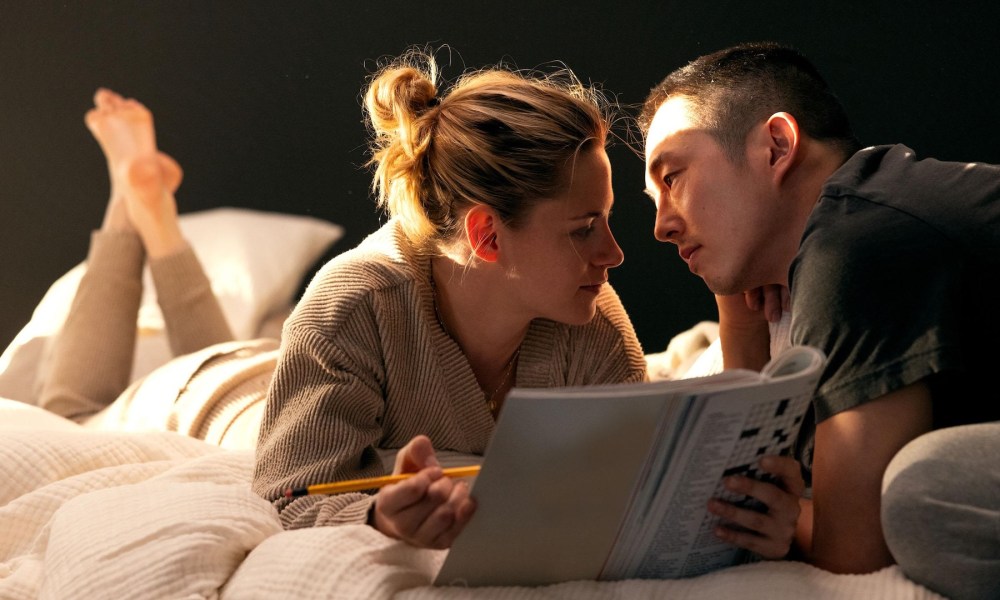 A woman and a man stare at each other while on a bed in Love Me.