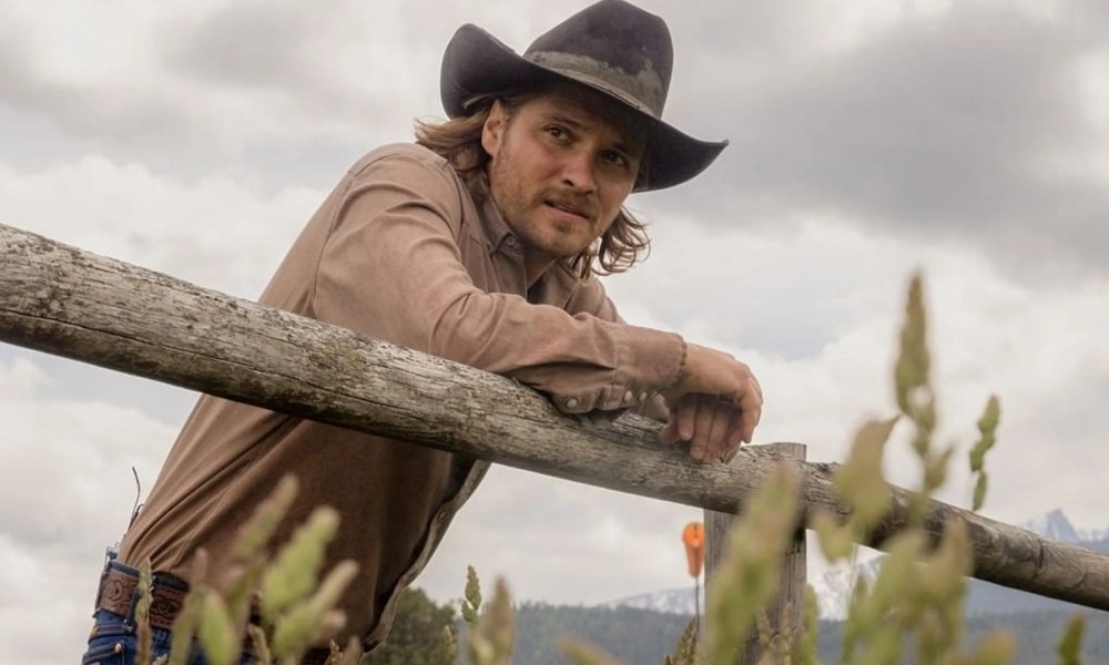 Luke Grimes leaning on a fence in Yellowstone.