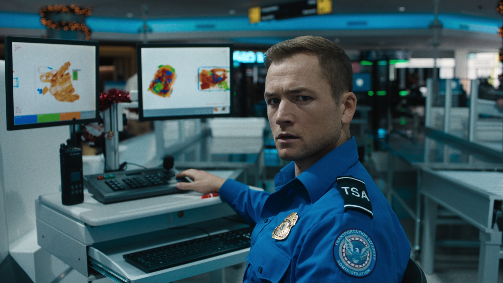 Taron Egerton sits at a desk and looks back in Carry-On.