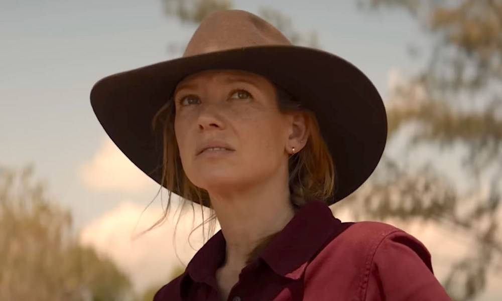 A woman in a cowgirl hat stares in Territory.