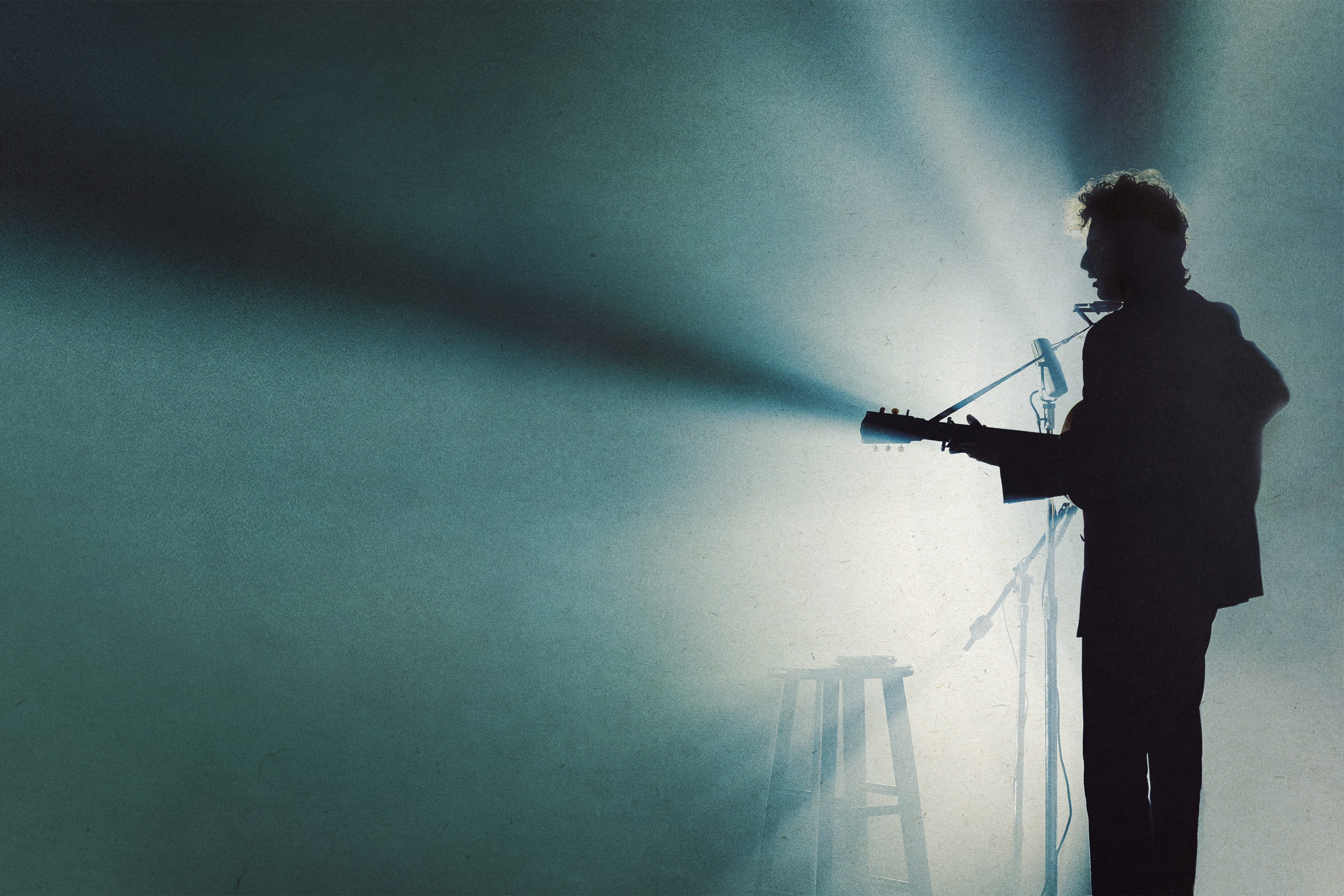 Timothée Chalamet stands in front of a microphone and spotlight in A Complete Unknown.