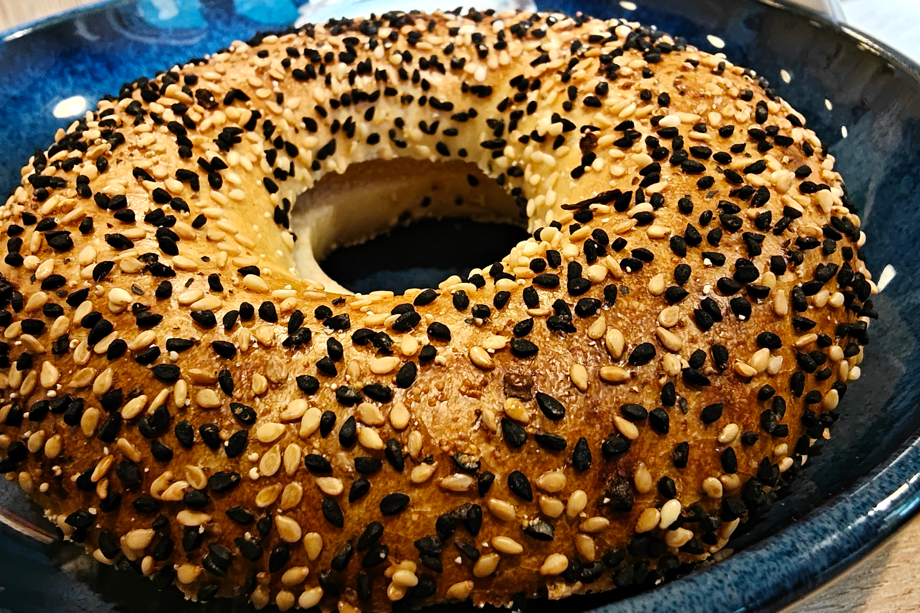 Un bagel de sésamo reposando en un plato azul.