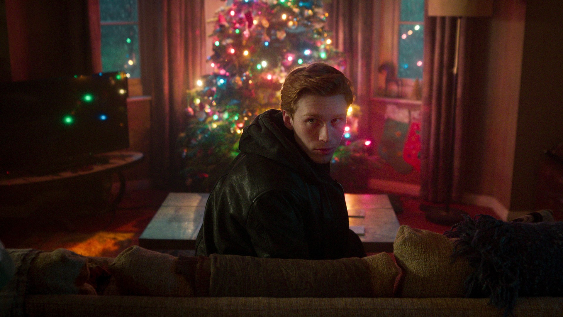 A man sits on a couch in Black Doves.