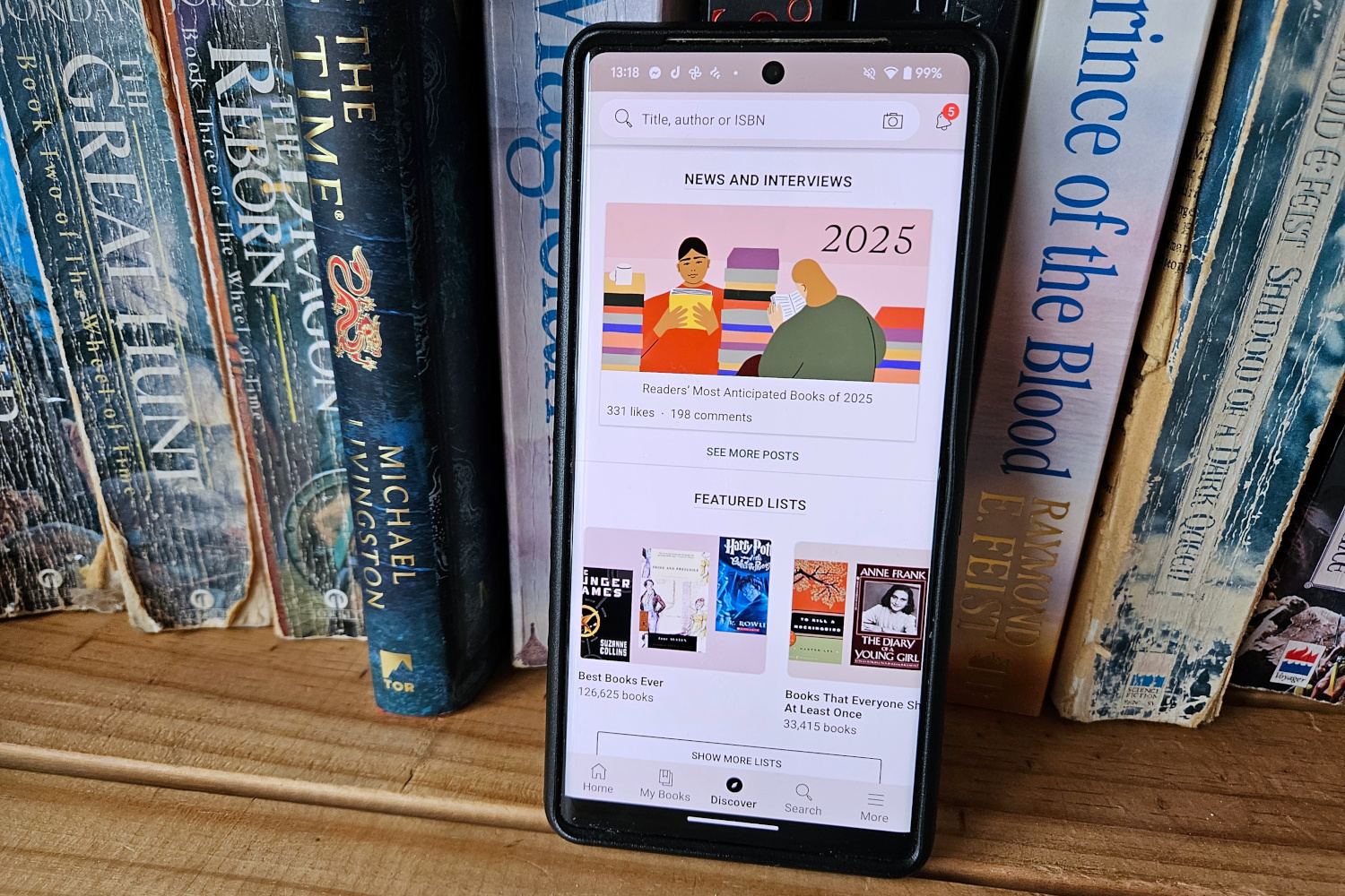 The GoodReads app open on a phone leaning against a row of books.