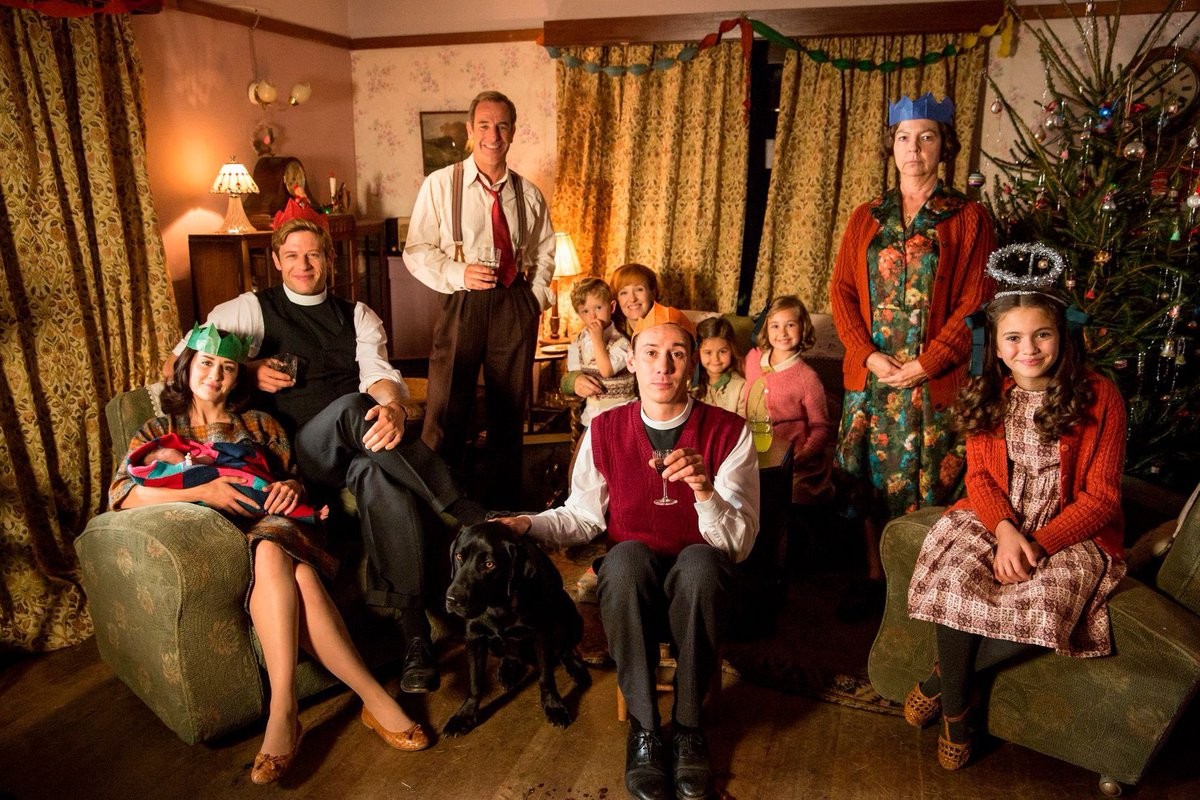 A group of people sit in a living room in Grantchester.