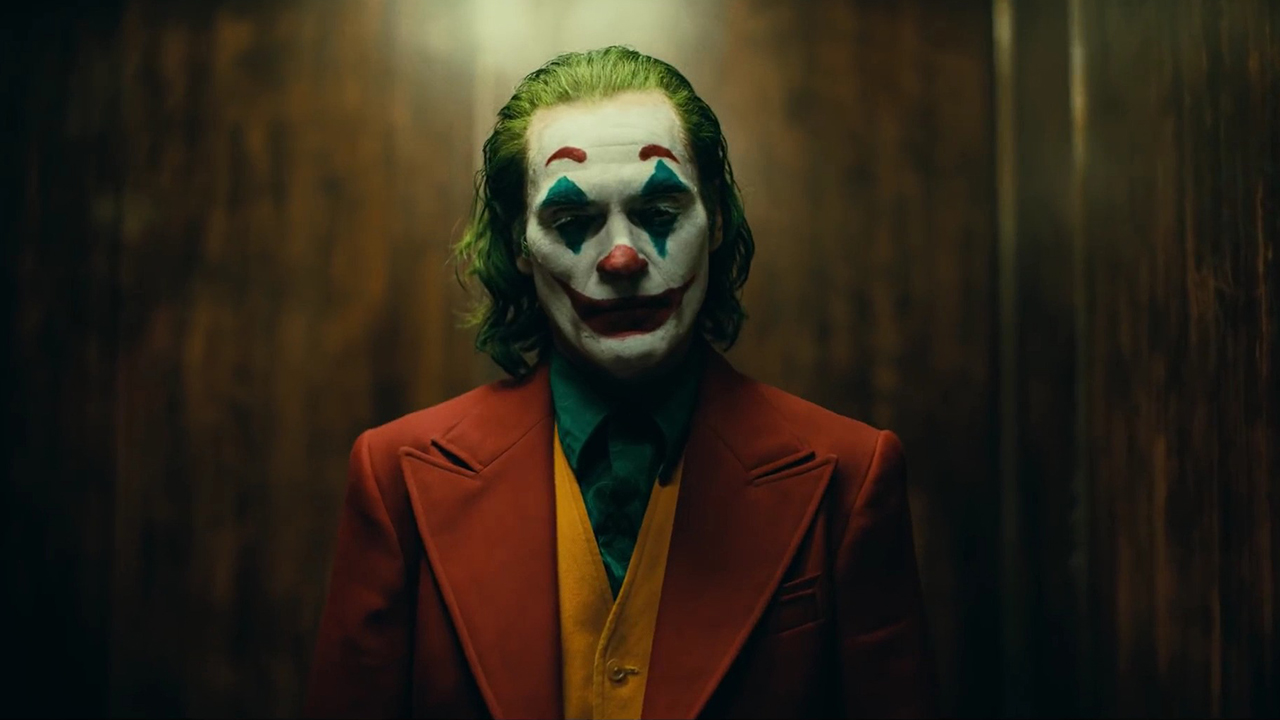 Arthur Fleck in Voll-Make-up steht in einem Aufzug und blickt in „Joker“ nach unten.