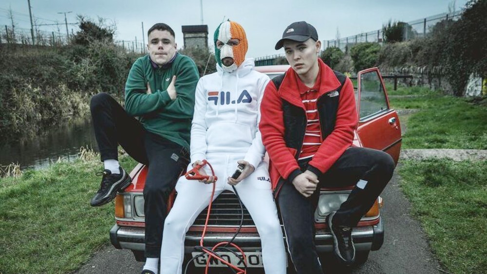 Three men sit on a car in Kneecap.