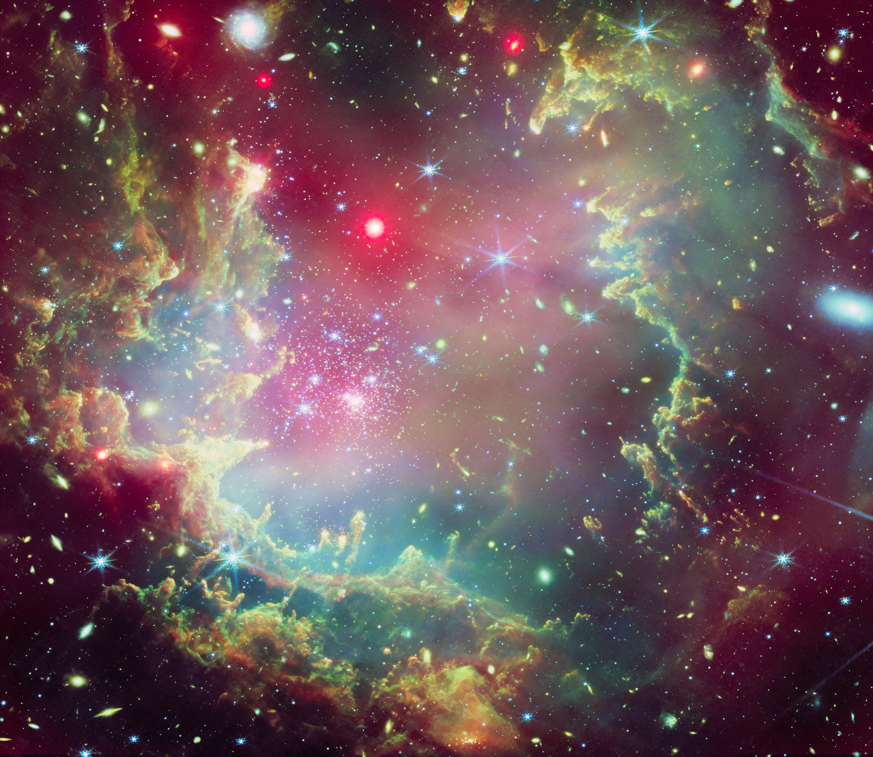 Dieses Bild zeigt den Sternhaufen NGC 602 in leuchtenden und festlichen Farben. Der Cluster umfasst einen riesigen Staubwolkenring, der in Grün-, Gelb-, Blau- und Orangetönen dargestellt ist. Die grünen Farbtöne und die gefiederten Ränder der Ringwolke erwecken den Eindruck eines Kranzes aus immergrünen Zweigen. Rote Andeutungen, die Röntgenstrahlen darstellen, sorgen für Schattierung und heben Schichten innerhalb der kranzartigen Ringwolke hervor.