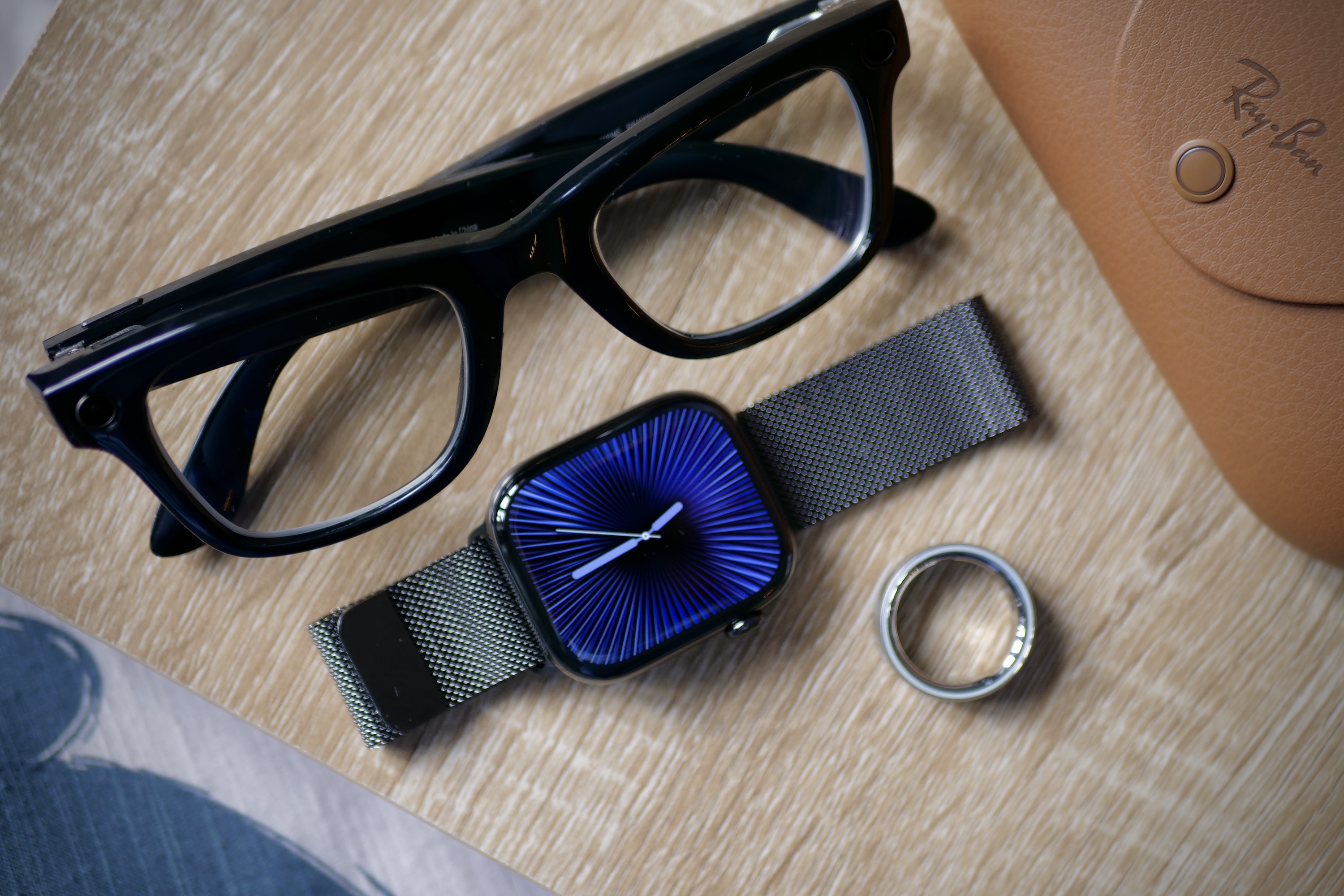 Os óculos inteligentes Ray-Ban Meta, Apple Watch Series 10 e Oura Ring 4 em uma mesa.