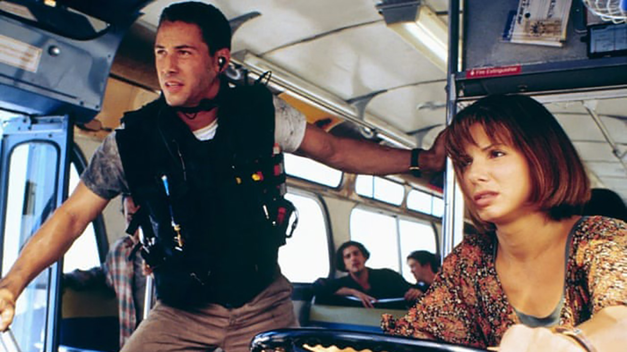 Keanu Reeves porte un gilet pendant que Sandra Bullock monte dans un bus dans Speed.