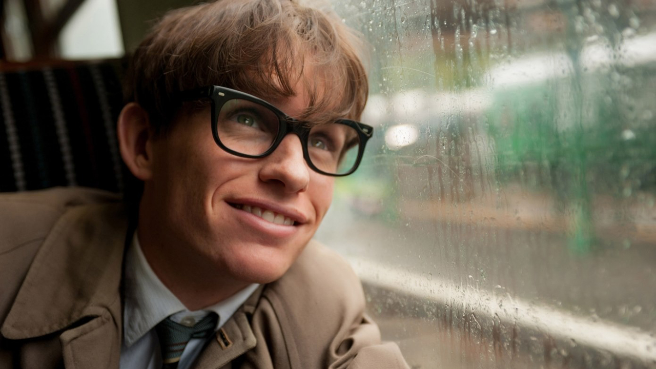 Um close de Eddie Redmayne como Stephen Hawking olhando pela janela de um veículo e sorrindo em A Teoria de Tudo.