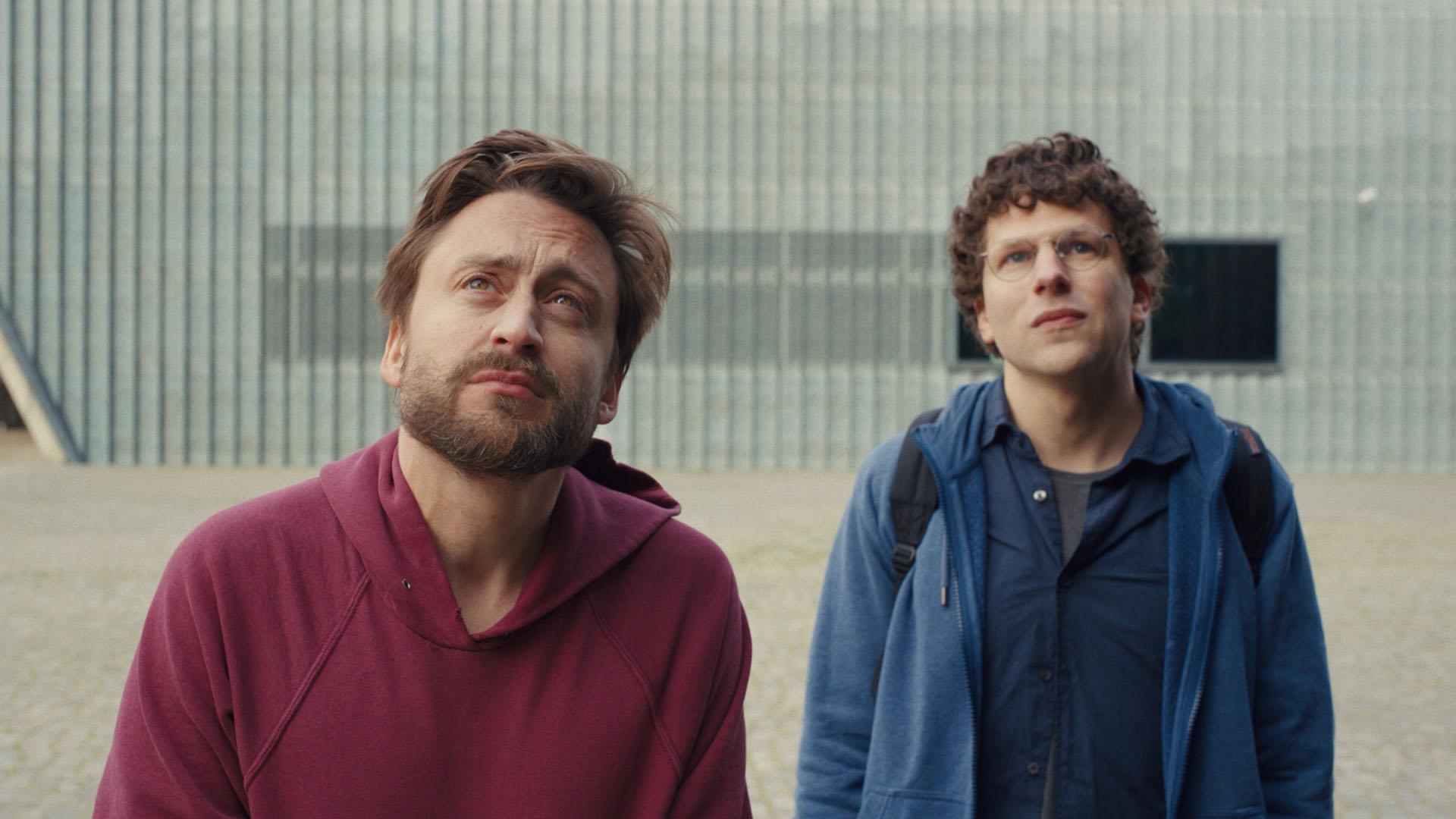 Kieran Culkin and Jesse Eisenberg stare at something in a still from the movie A Real Pain.