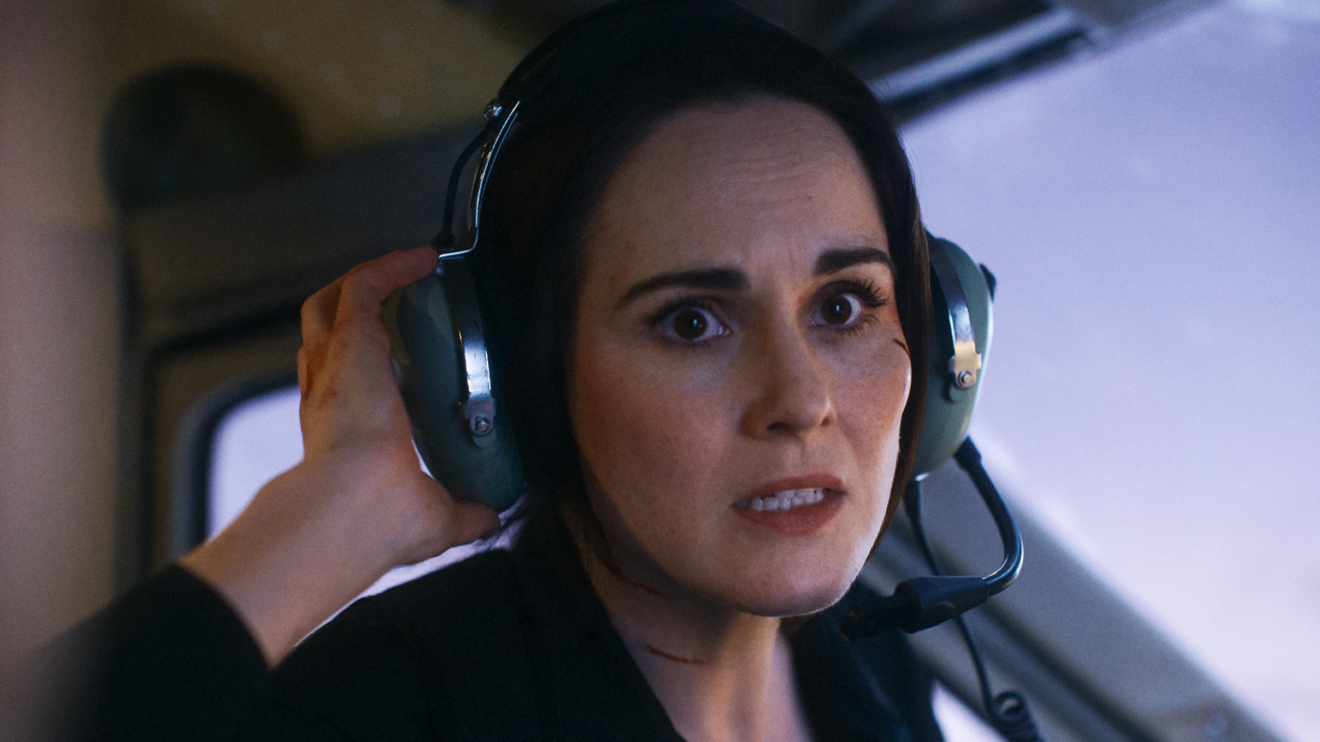 Michelle Dockery sieht in einem Standbild aus dem Film Flight Risk mit aufgesetztem Flugzeug-Headset panisch aus.