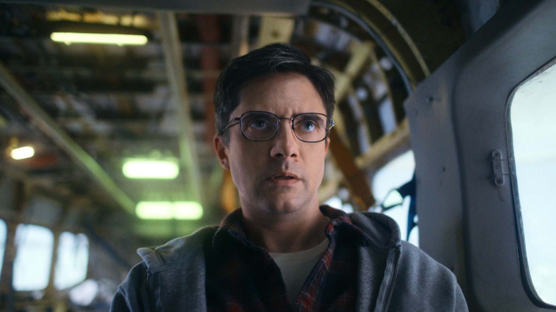 Topher Grace sits in an airplane looking alarmed in a still image from the movie Flight Risk.