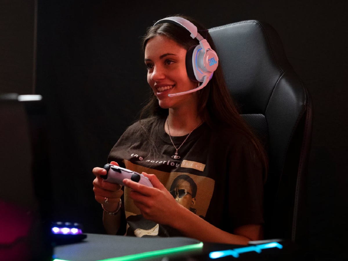 A woman with the PS5 controller wearing the JBL Quantum 910P gaming headset.