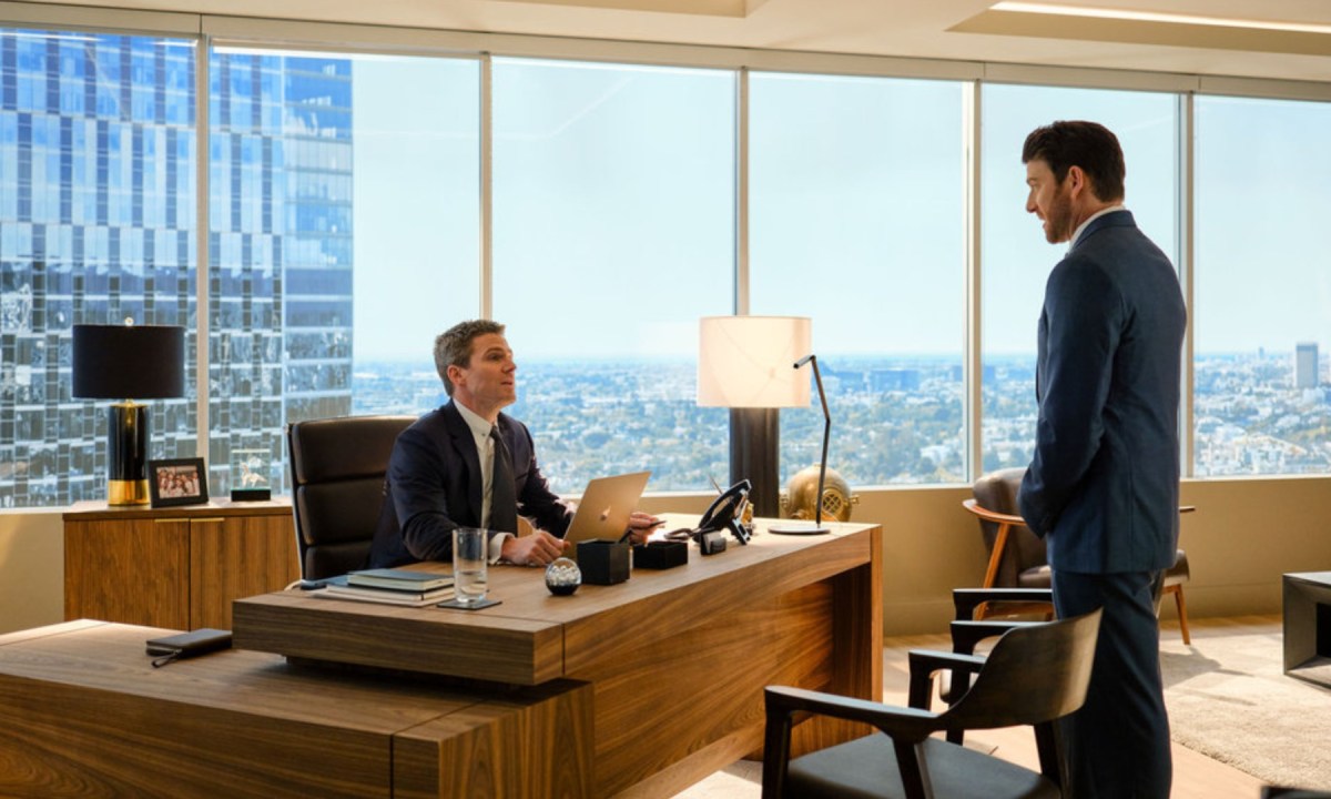 A man sits at his desk as another one stands in front of it in Suits LA.