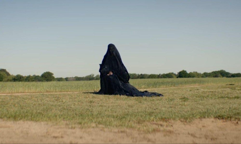 A woman draped in black sits in a yard.