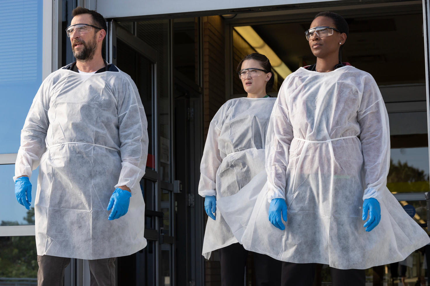 Three doctors stand together near an open doorway in The Pitt.