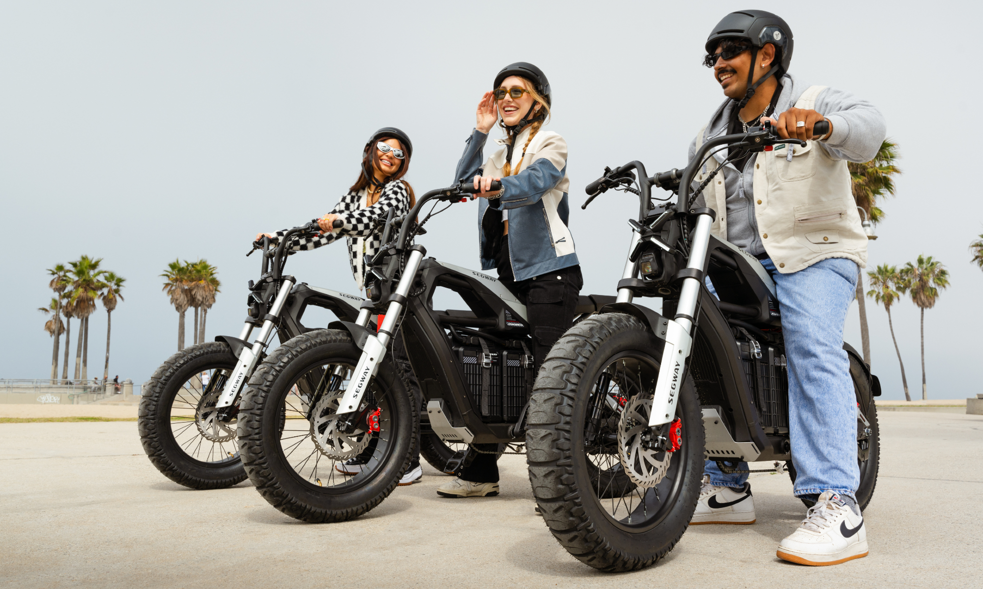 Trois personnes sur des vélos électriques Segway Xyber près de la plage avec des palmiers en arrière-plan.