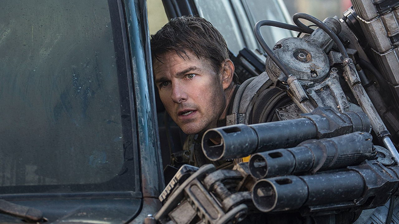 Tom Cruise de uniforme apoyado contra un coche en Al filo del mañana.