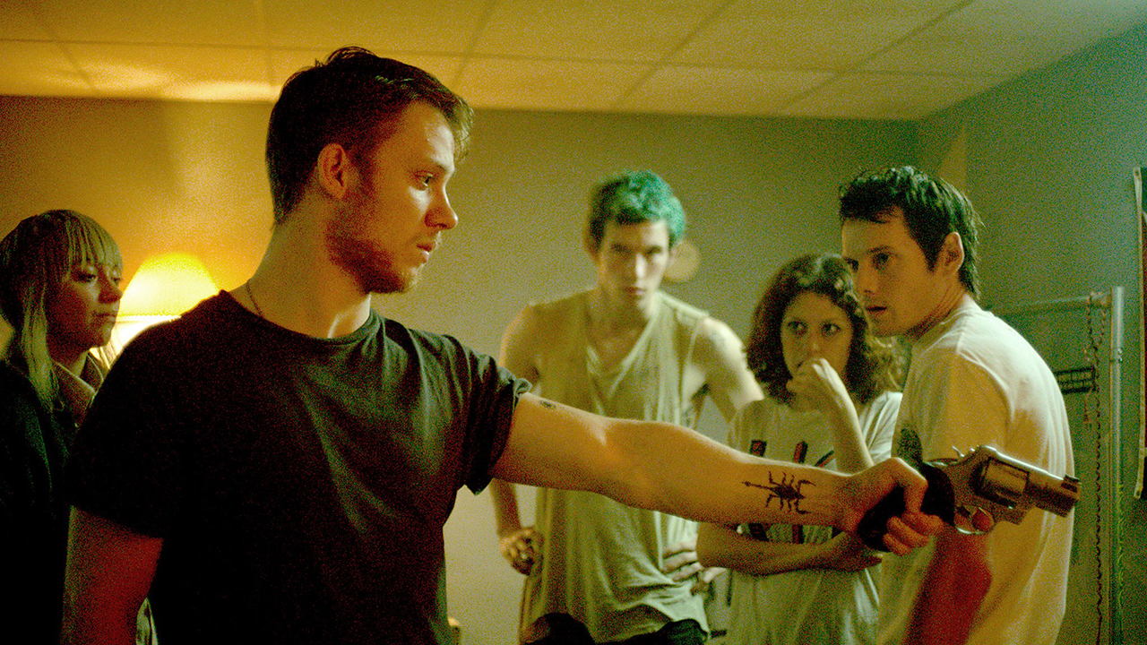 Several people in a room, one holding a gun out pointed to the right in Green Room.