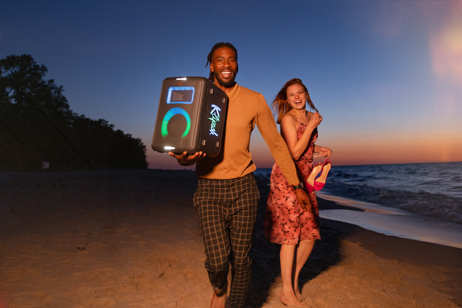 L'orateur de la fête Klipsch Vegas est tenu par un homme marchant sur une plage avec une femme.